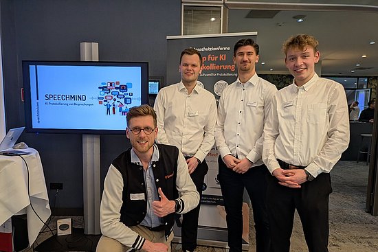 Vier junge Männer präsentieren SpeedMind KI-gestützte Sitzungsprotokollierung auf einer Messe